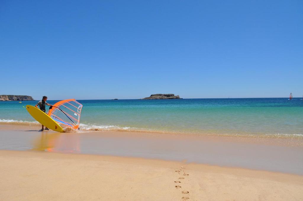 a person is standing on the beach with a surfboard at Martinhal Sagres Beach Family Resort Hotel in Sagres