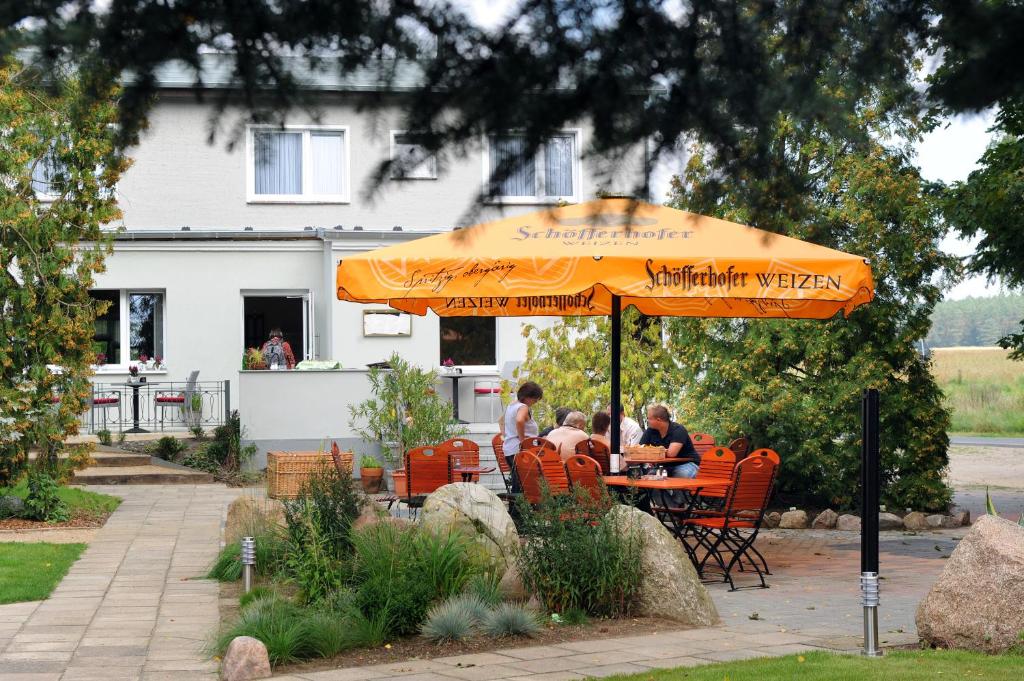 Un groupe de personnes assises à une table sous un parapluie orange dans l'établissement Hotel Zum Birkenhof, à Burow