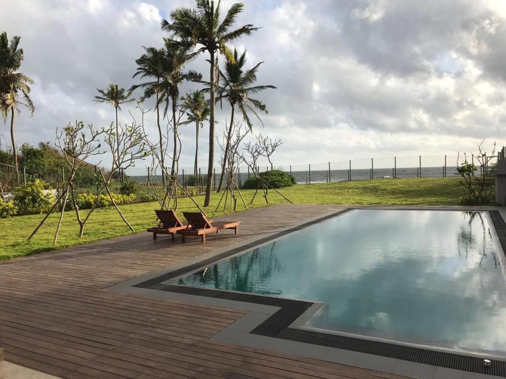 a swimming pool with two chairs and palm trees at Villa by the Sea, Negombo-Katunayake in Pamunugama