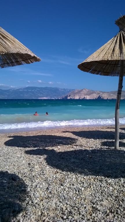 a beach with two umbrellas and people in the water at Lovrić Apartments in Baška