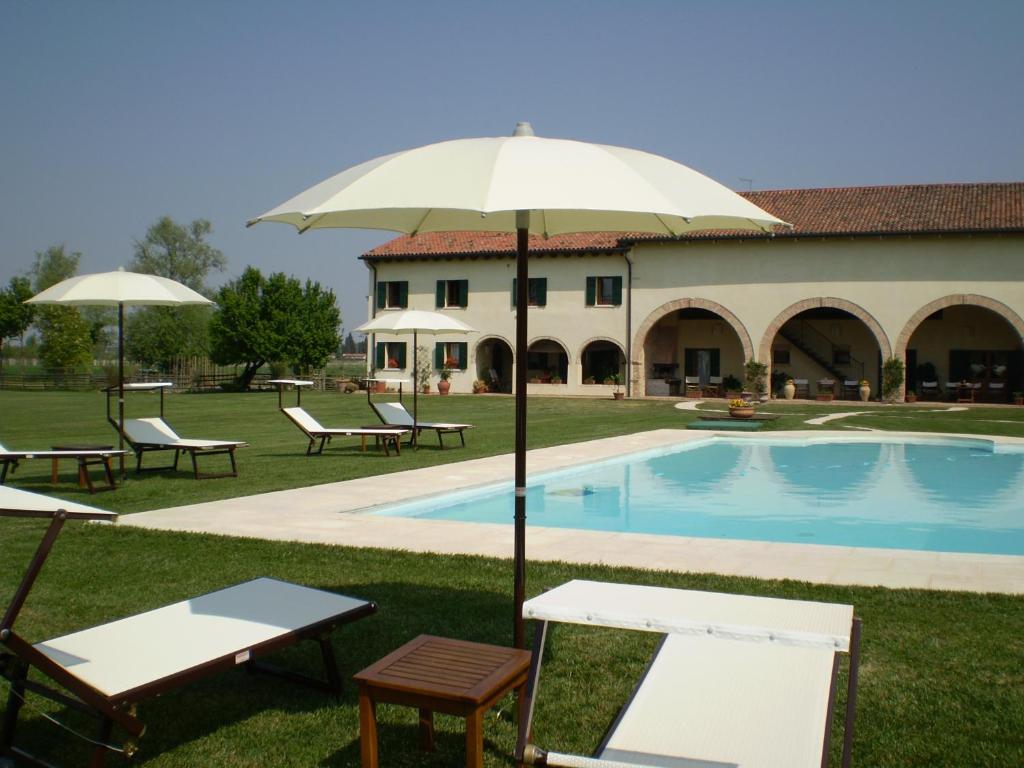 a pool with chairs and an umbrella next to a building at Il Rifugio del Poeta in San Biagio di Callalta