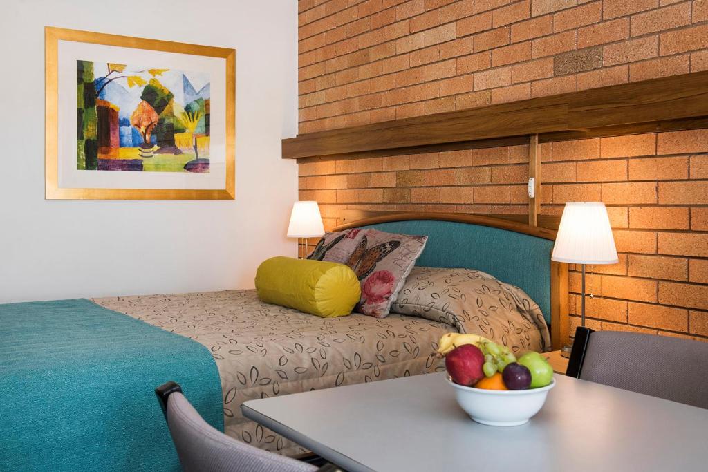 a room with a bed and a table with a bowl of fruit at Ningana Motel in Mudgee