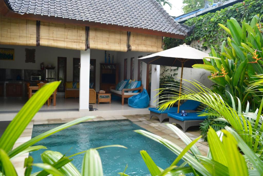 a pool in front of a house with an umbrella at Villa Mewali in Ubud