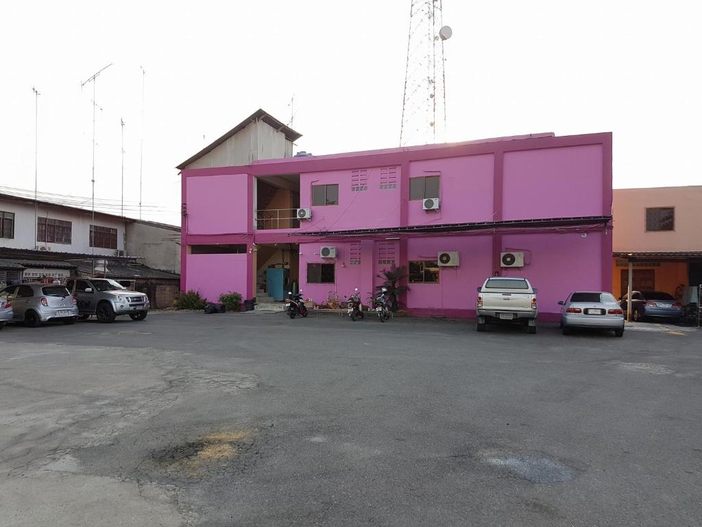 a pink building with cars parked in a parking lot at Charinsup Hotel in Ban Khlong Thai Muang