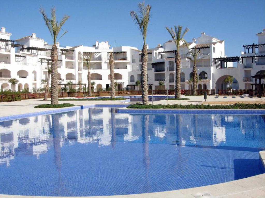 a swimming pool in front of a building with palm trees at Coming Home - Penthouses La Torre Golf Resort in Roldán