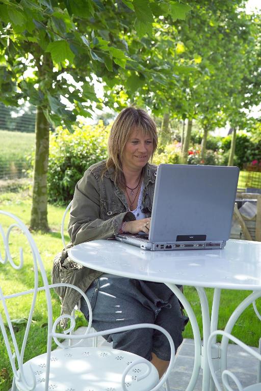 a woman sitting at a table with a laptop at Côte d&#39;Opale - La Ferme des Saules in Millam