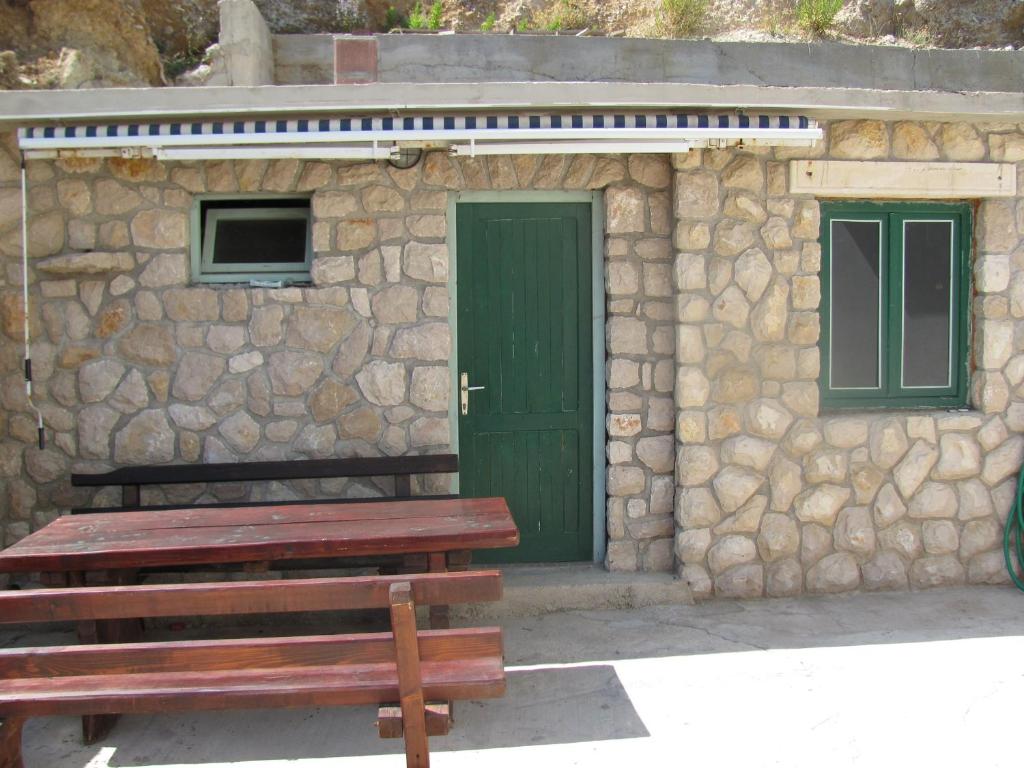 a stone building with a green door and a bench at Apartments Alaburic in Pag