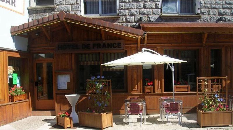 a building with an umbrella and tables and chairs at Hôtel de France in Le Bessat