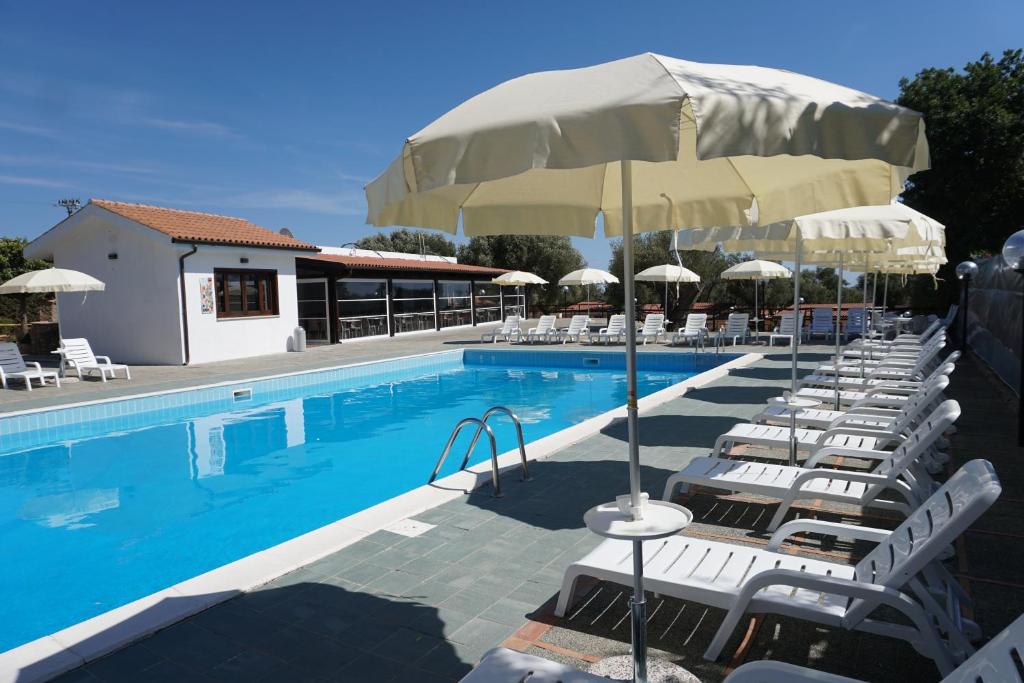 een zwembad met witte stoelen en een parasol bij Cilento Dreams Village in Marina di Camerota