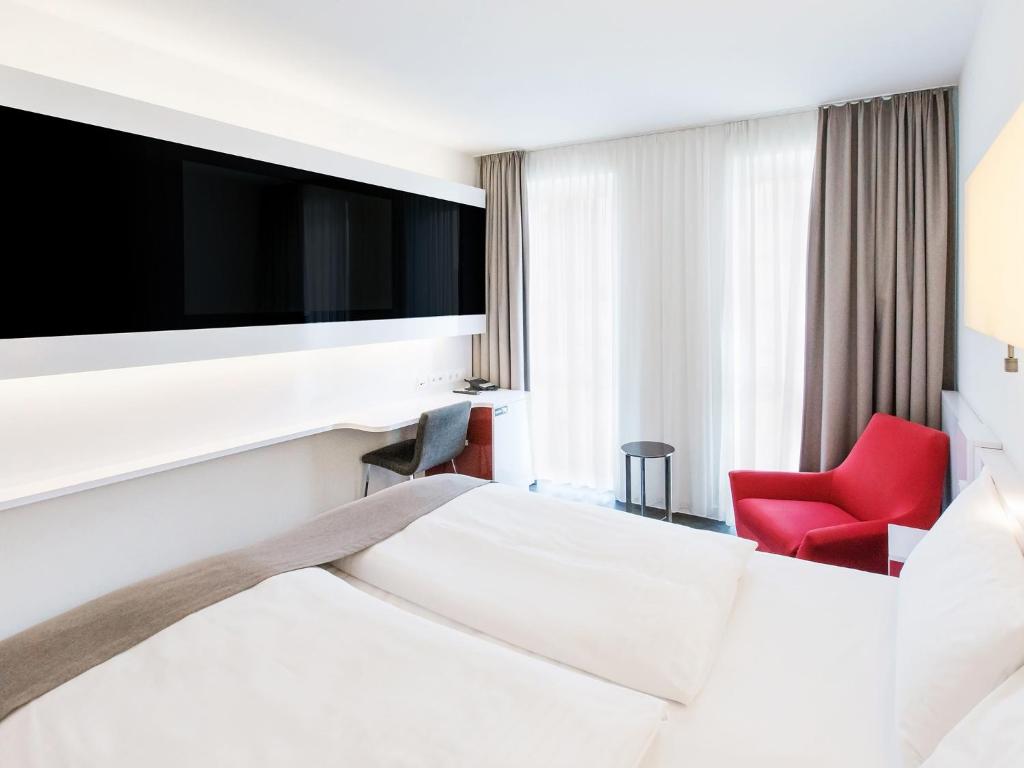 a hotel room with a bed and a red chair at DORMERO Hotel Frankfurt in Frankfurt/Main