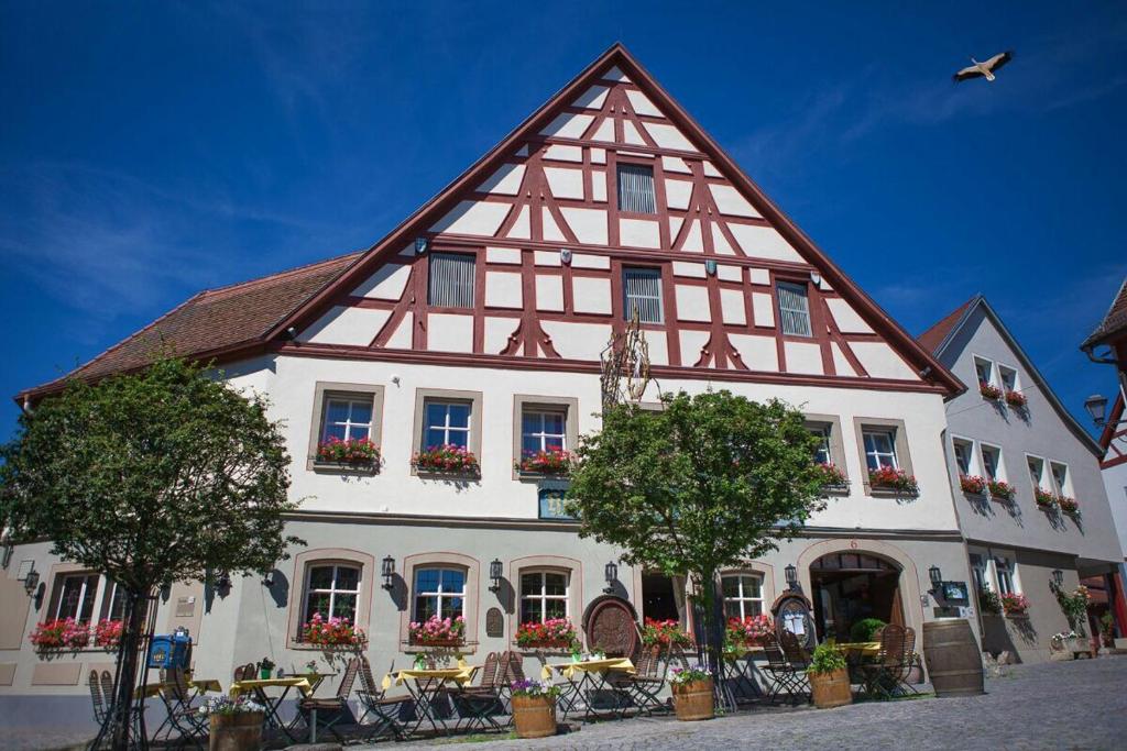 ein großes weißes und rotes Gebäude mit Tischen und Bäumen in der Unterkunft Flair Hotel zum Storchen in Bad Windsheim