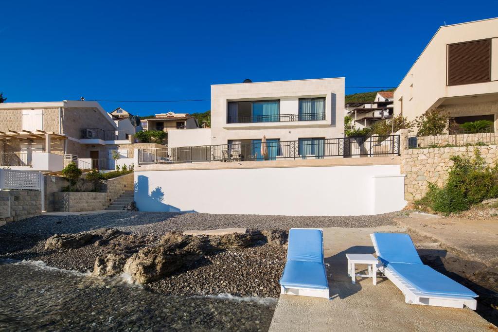 two blue lounge chairs on the beach in front of a house at Villa Krasici in Tivat