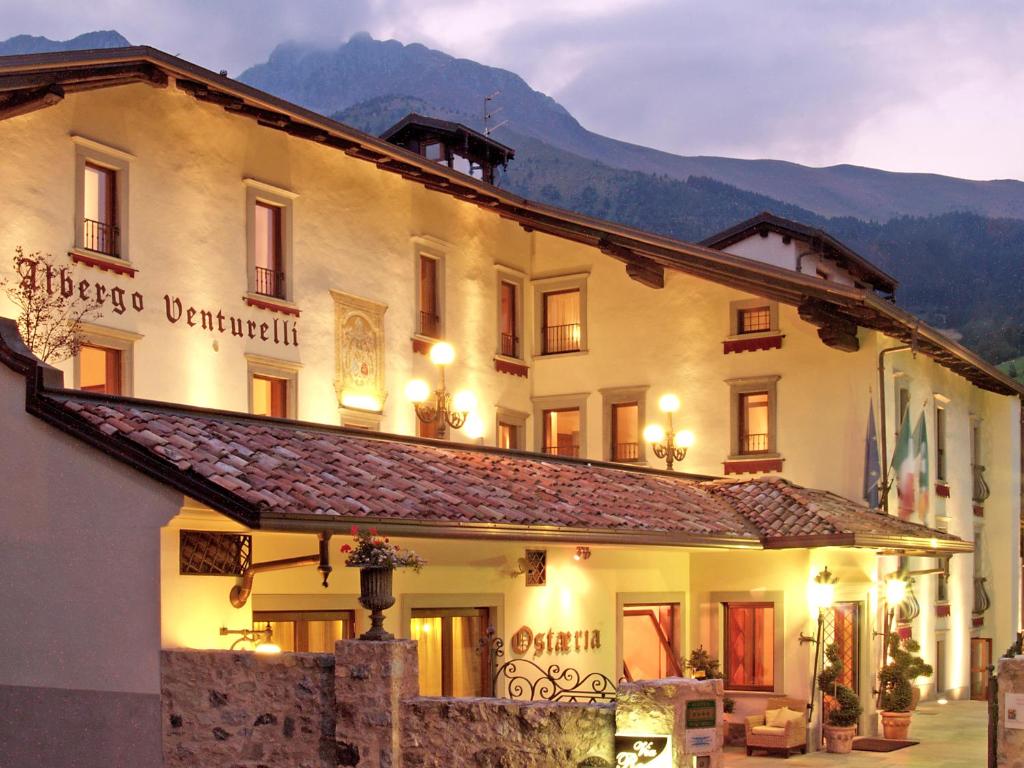 a large white building with mountains in the background at Albergo Venturelli in Borno