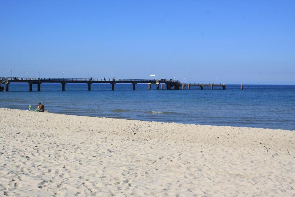 eine Person, die am Strand mit einem Pier im Wasser sitzt in der Unterkunft Haus Strandeck Apartment Meeresrauschen 12 in Göhren