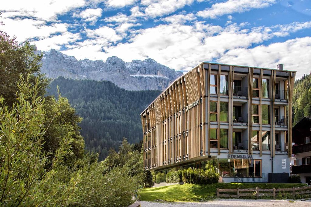 um edifício de madeira com montanhas ao fundo em Mountain Design Hotel EdenSelva em Selva di Val Gardena