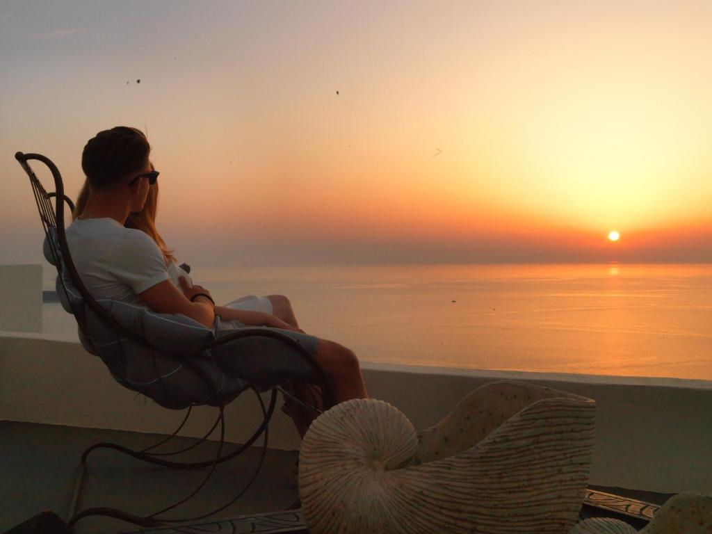 a man and woman sitting in a chair watching the sunset at OIA UNIQUE HOMES by K&K in Oia