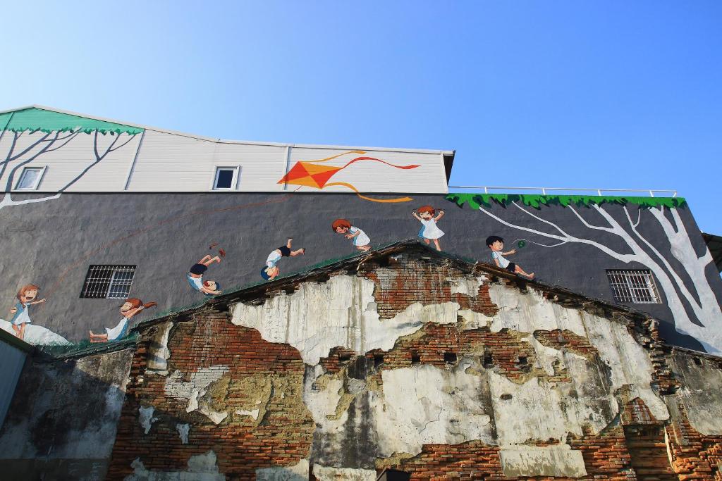 a mural of people on the side of a building with a kite at Bao Cheng Home in Tainan