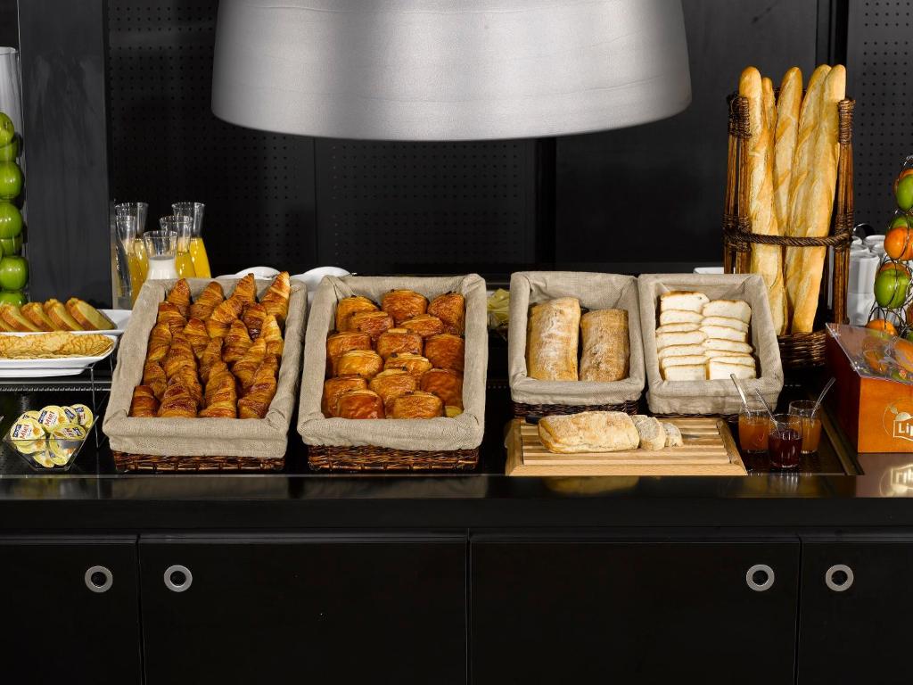 - un buffet avec plusieurs plateaux de viennoiseries et de pain dans l'établissement Campanile Lille - Lomme, à Lomme