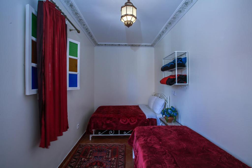 two beds in a room with red curtains and a lamp at Hotel Zaitoune in Marrakech