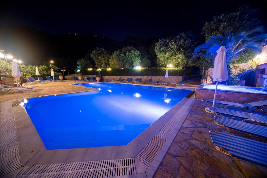una piscina por la noche con sillas y sombrillas en Arianna, en Paleokastritsa