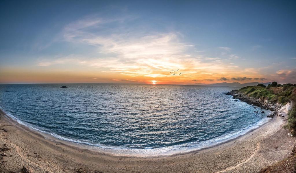 una puesta de sol sobre el océano con una playa de arena en Dionisos Hotel, en Mitikas