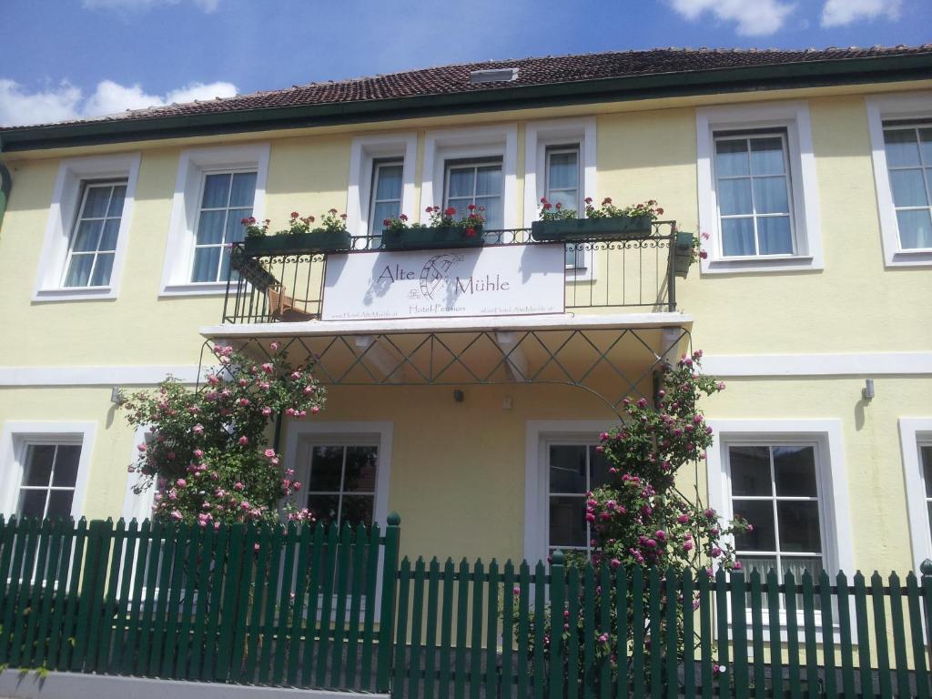 żółty dom z kwiatami na balkonach i płotem w obiekcie Hotel Pension Alte Mühle w mieście Klosterneuburg
