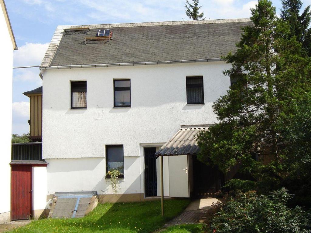 une maison blanche avec un arbre en face dans l'établissement Zimmervermietung-Heide-Fiege, à Hartmannsdorf