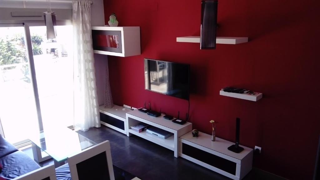 Elle comprend un salon doté d'un mur rouge et d'une télévision. dans l'établissement Apartamento Puerto Real, à Torremolinos