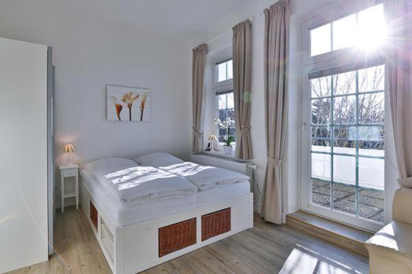 a white bedroom with a bed and a large window at Appartement-5-mit-Suedbalkon-in-strandnaher-Lage-Baederstil-Villa-in-Wenningstedt-Sylt in Wenningstedt