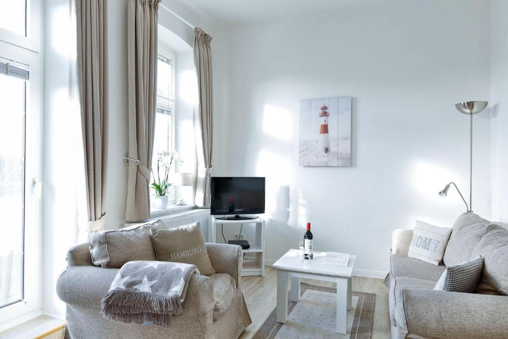 a white living room with two chairs and a tv at App-6-mit-Suedbalkon-in-strandnaher-Lage-Baederstil-Villa-in-Wenningstedt-Sylt in Wenningstedt