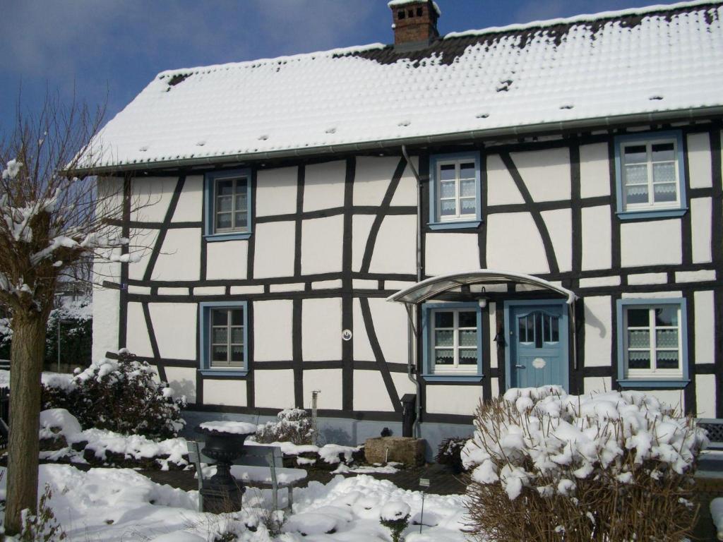 a white house with a blue door in the snow at Haus-Hoeppches in Blankenheim