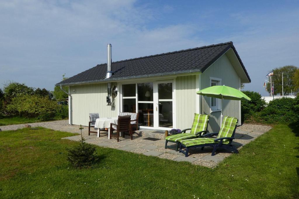 ein Haus mit zwei Stühlen und einem grünen Regenschirm in der Unterkunft Ferienhaus Silbermöwe in Kappeln