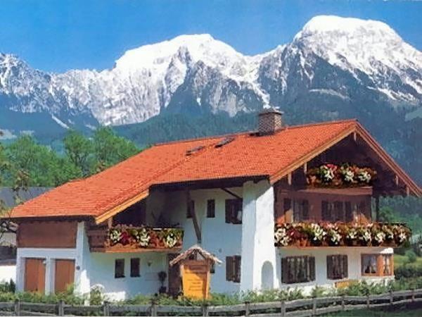 ein Haus mit einem orangenen Dach mit Bergen im Hintergrund in der Unterkunft Landhaus Haid Fewo Enzian in Schönau am Königssee