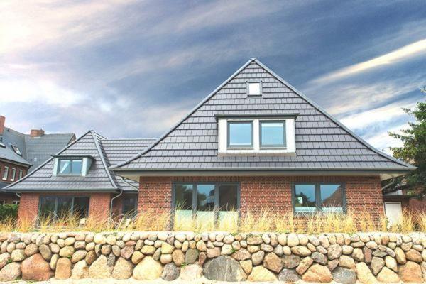 een huis met een gambrel dak en een stenen muur bij Strandkoje-Landhaus-Tadsen in Westerland