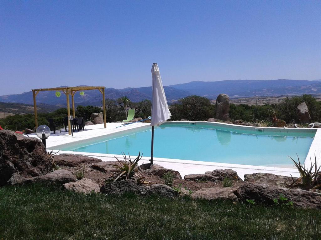 a large swimming pool with an umbrella in the grass at Country House Mura Mura in Sedini