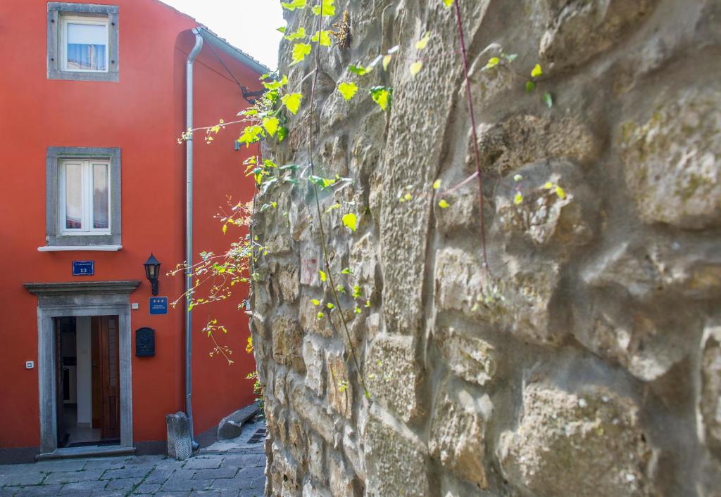 a red building and a stone wall with yellow flowers at Karla Apartment in Labin