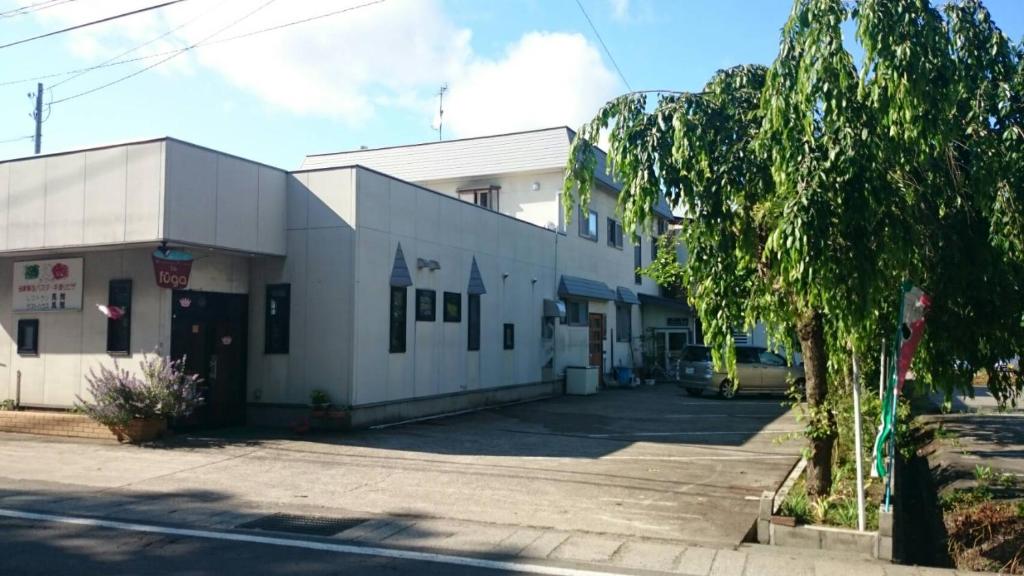 a white building with a parking lot next to a street at Kakunodate Guesthouse Fuga in Senboku