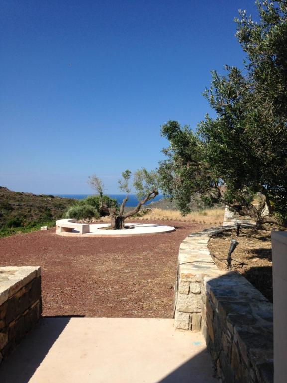 a garden with a stone wall and trees and the ocean at Studio Julie in Kapsali