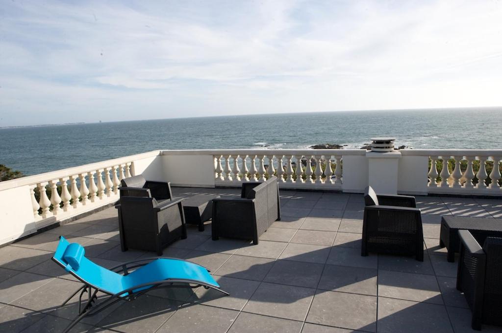 uma varanda com uma cadeira azul e mesas e o oceano em Villa Belmont em La Turballe