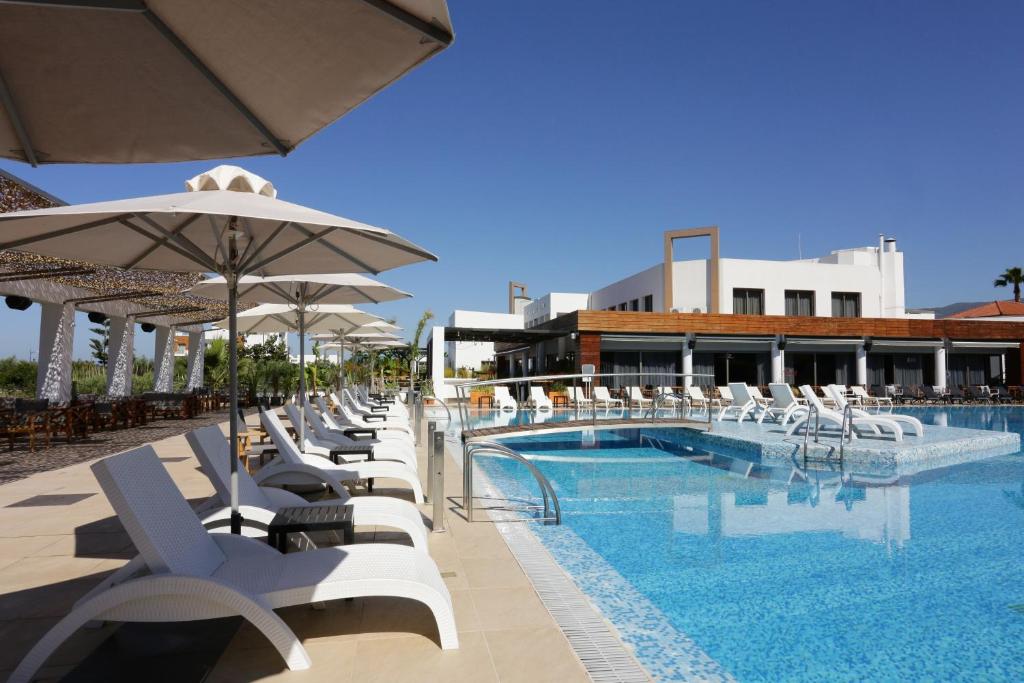 a swimming pool with white chairs and umbrellas at Elite City Resort in Kalamata