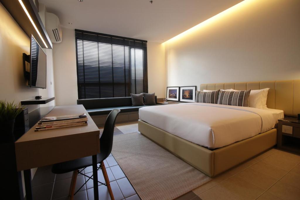 A furnished bedroom with a king-size-looking bed, desk, TV and window seat.