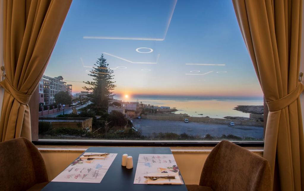 a table with chairs and a window with a view of the ocean at Vivaldi Hotel in St. Julianʼs