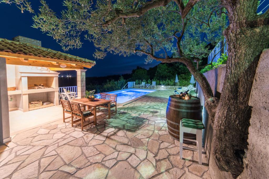 un patio con una mesa, un árbol y una piscina en Olive Garden Apartments, en Čilipi