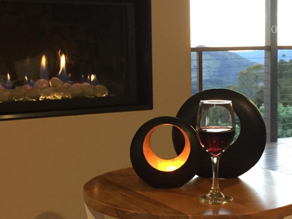 una copa de vino en una mesa con chimenea en Blue Summit Cottages en Maleny