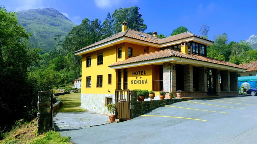 un edificio amarillo en un estacionamiento junto a una montaña en Hotel Benzua, en Villanueva de Ardisana