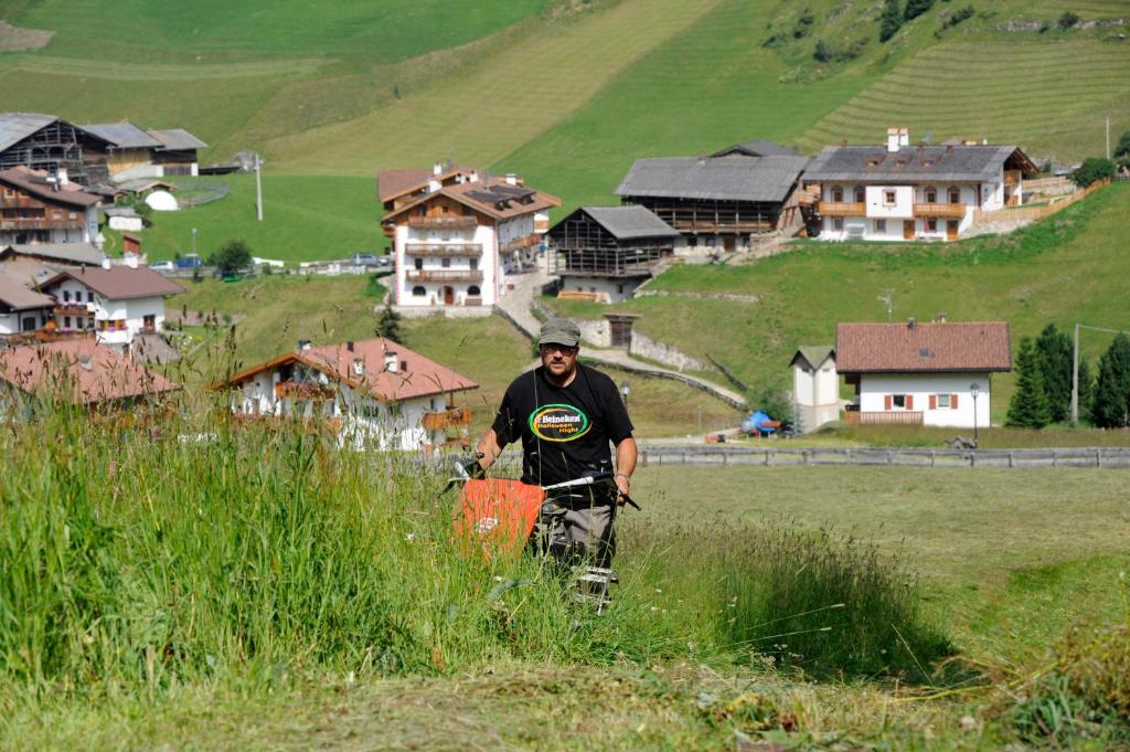 a man standing in a field of grass with houses at Agriturismo Maso Larciunei in Selva di Val Gardena