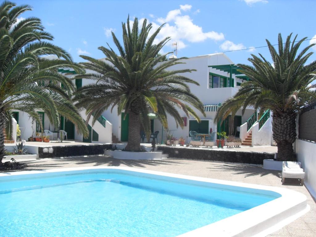 a swimming pool with palm trees in front of a building at Irene Apartment in Puerto del Carmen