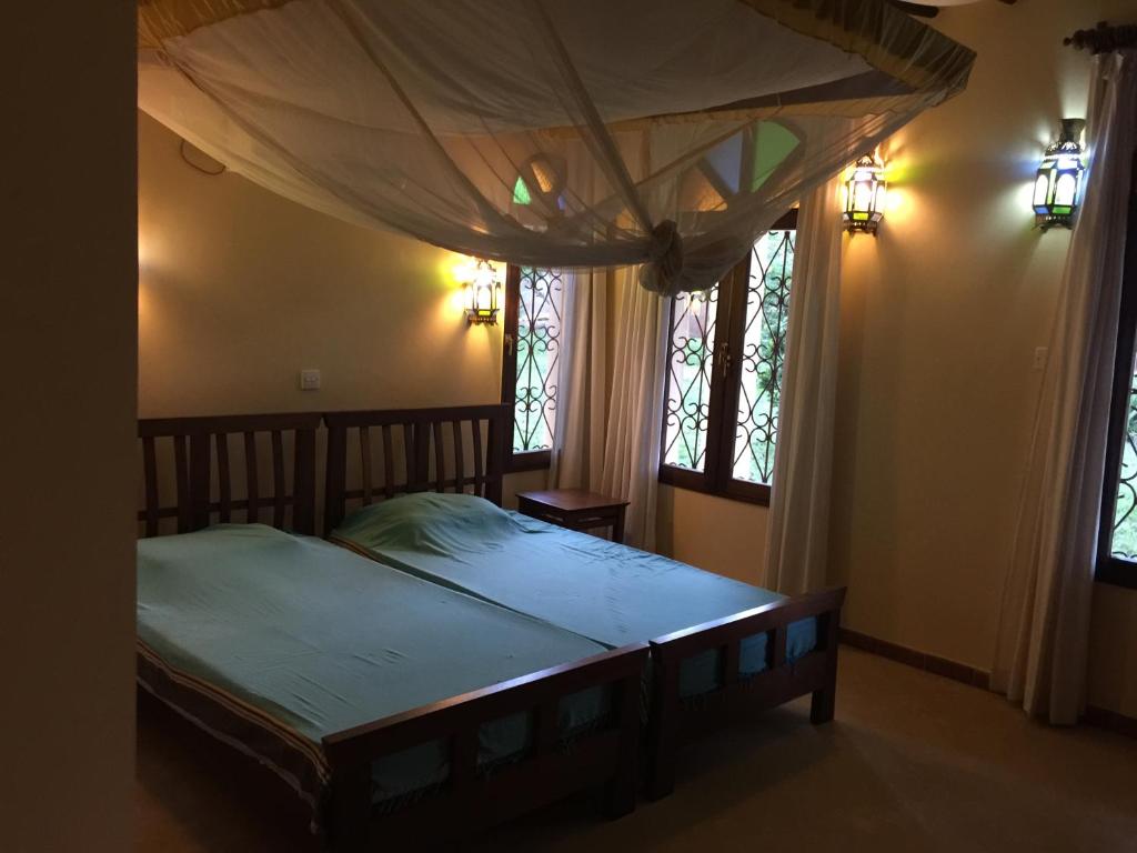 a bedroom with a canopy bed with two windows at Marula Park in Diani Beach