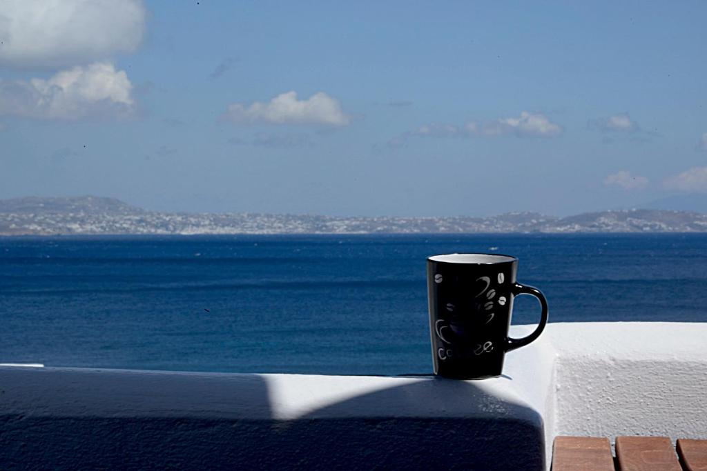 a black coffee mug sitting on a ledge overlooking the ocean at Porto Vlastos in Agios Ioannis