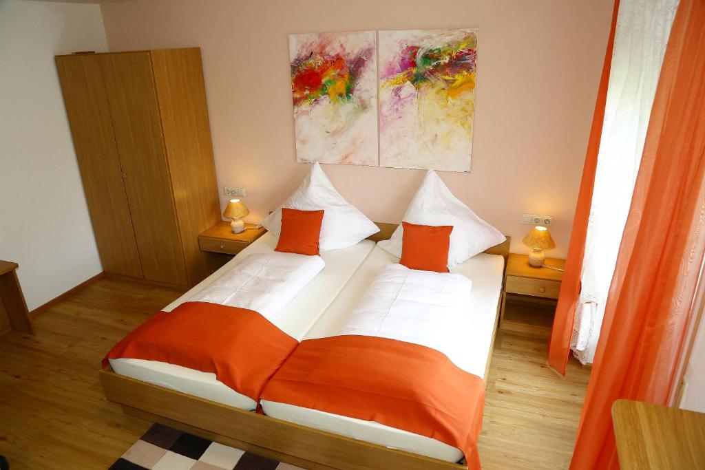 Landhotel Garni Schweizerhaus في سخونوالد: غرفة نوم مع سرير مع وسائد برتقالية وبيضاء